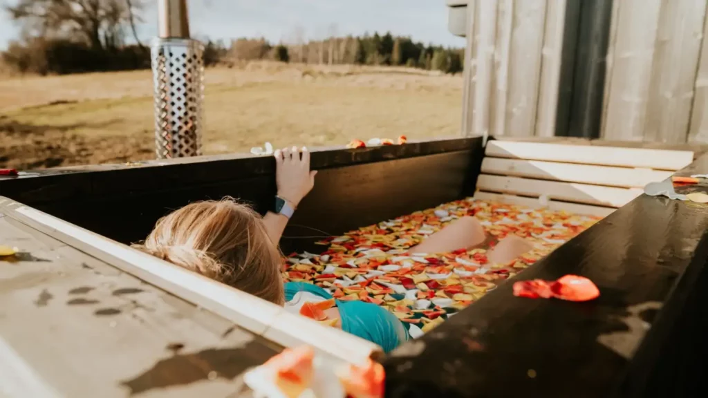 Kobieta relaksuje się w wodzie z płatkami róż w wannie ogrodowej